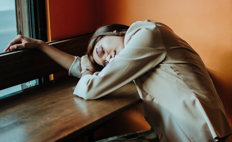 Woman in beige outfit leaning at a cafe table, embodying relaxation in a warm, cozy setting.