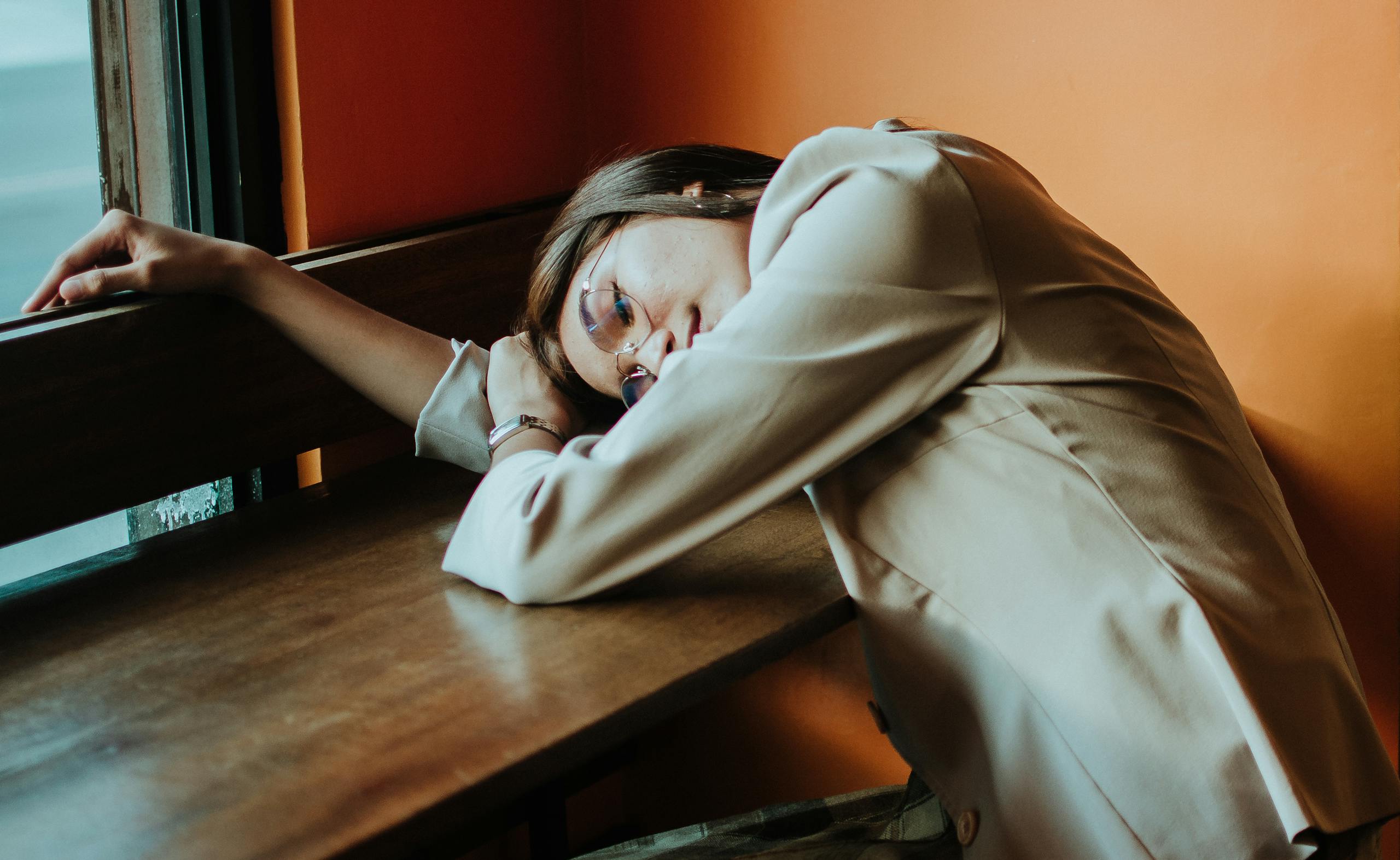 Woman in beige outfit leaning at a cafe table, embodying relaxation in a warm, cozy setting.