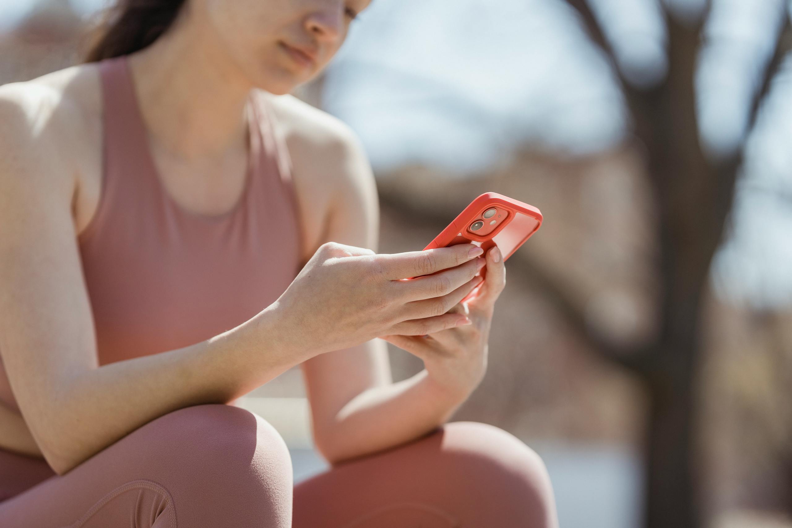 Woman in workout attire checking smartphone outdoors, enjoying a sunny day.
