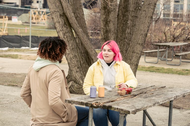 Woman with pink hair and faceless African American man sitting at wooden table with cans of soda and fresh strawberries