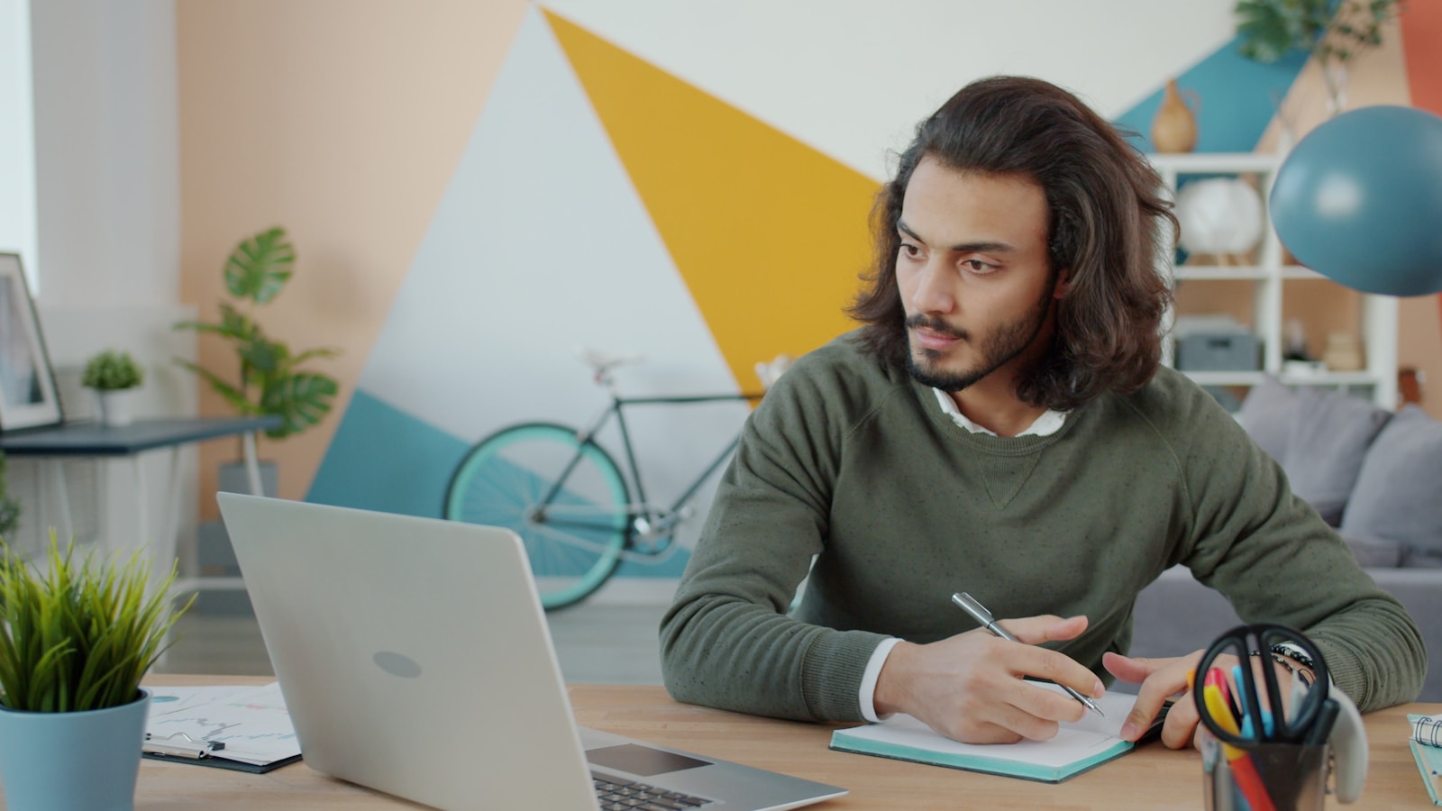 Man working at a desk with a laptop and notebook.