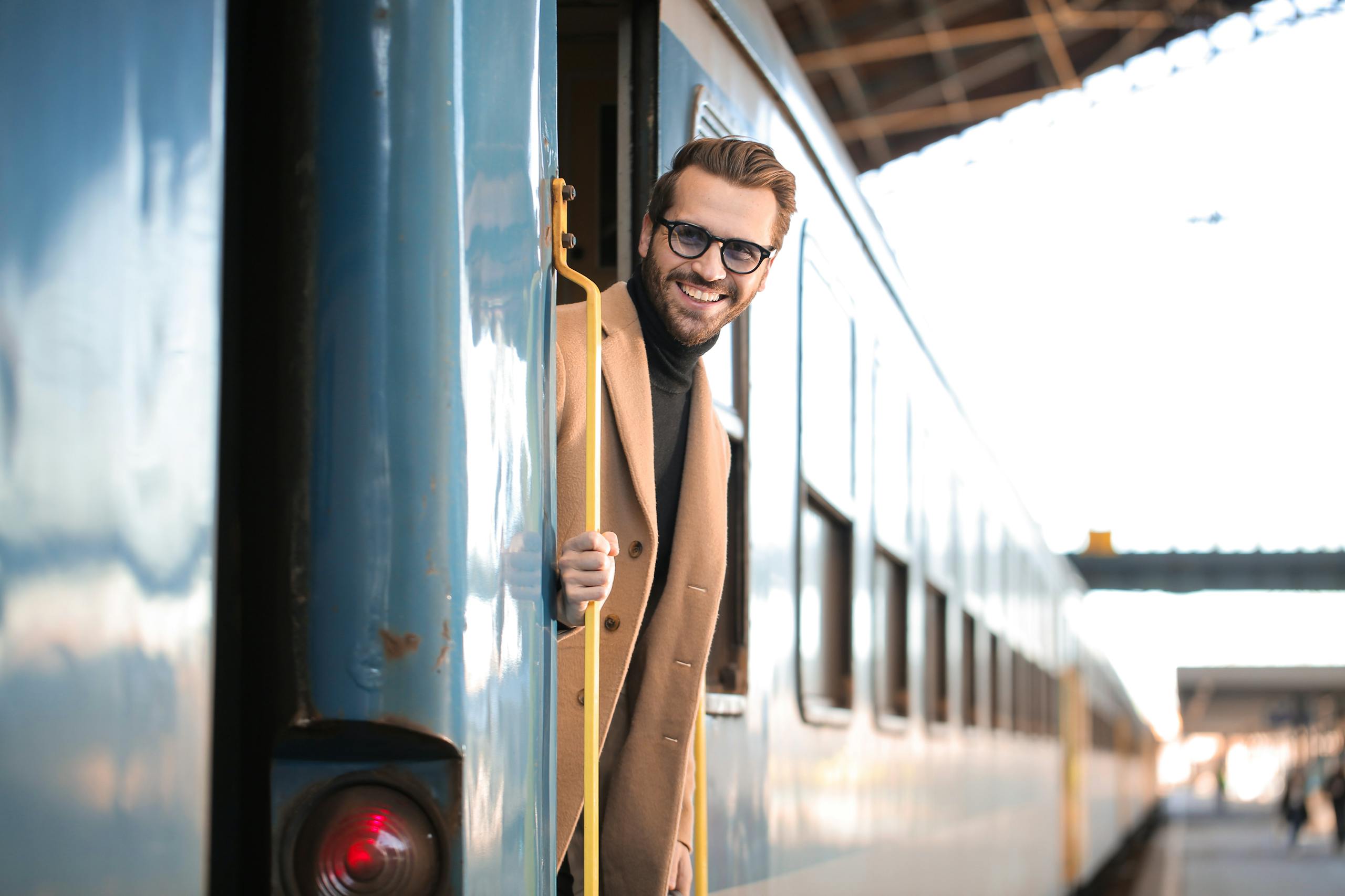 Young man with glasses smiles from train at Budapest railway station.