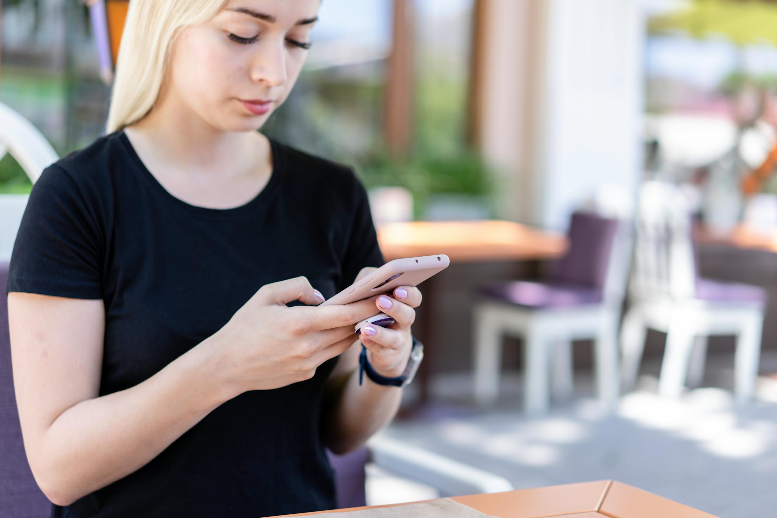 Young woman in a black shirt texting on her smartphone at an outdoor cafe.
