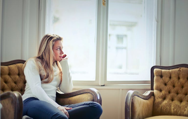 Young woman in a cozy armchair by a window, enjoying peaceful relaxation at home.