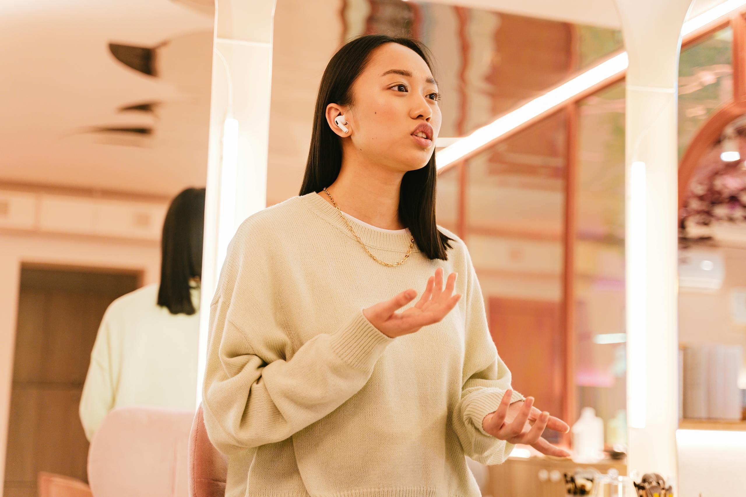 Young woman speaking passionately while wearing wireless earphones in a modern indoor setting.