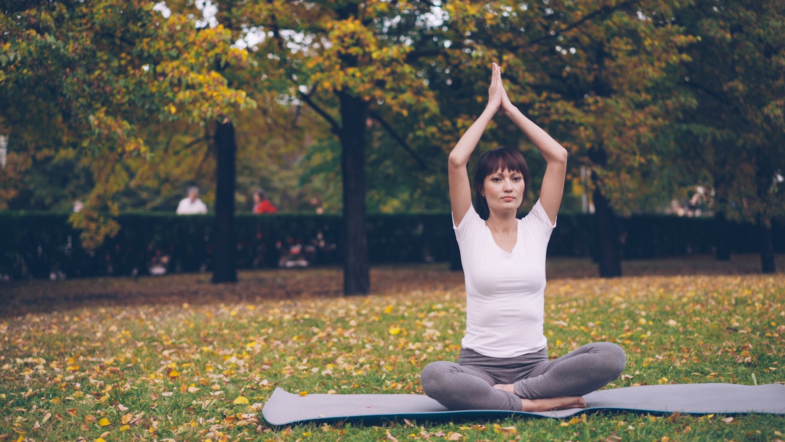 Woman meditating in a park with autumn trees.