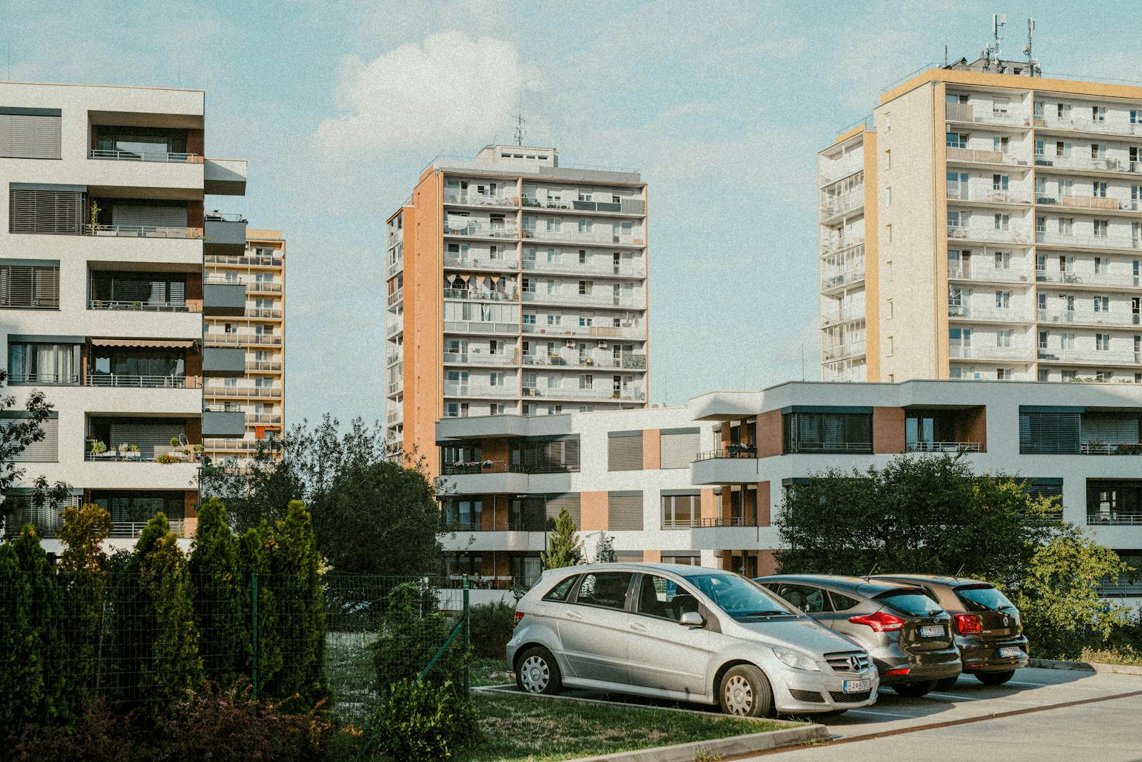 A scenic view of modern apartment buildings with cars parked in the foreground during a sunny day.