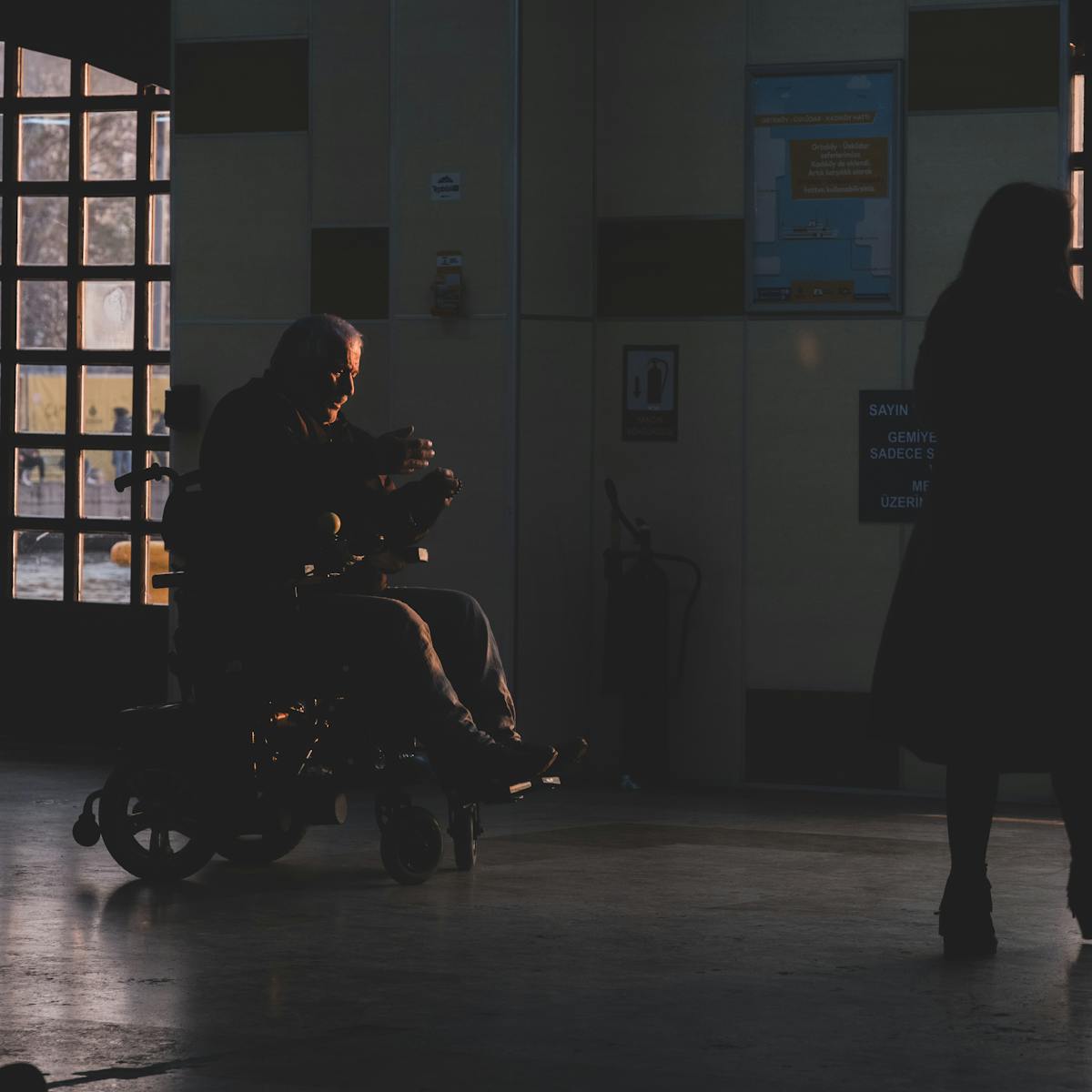 Silhouette of a person in a wheelchair inside a hospital corridor during sunset.