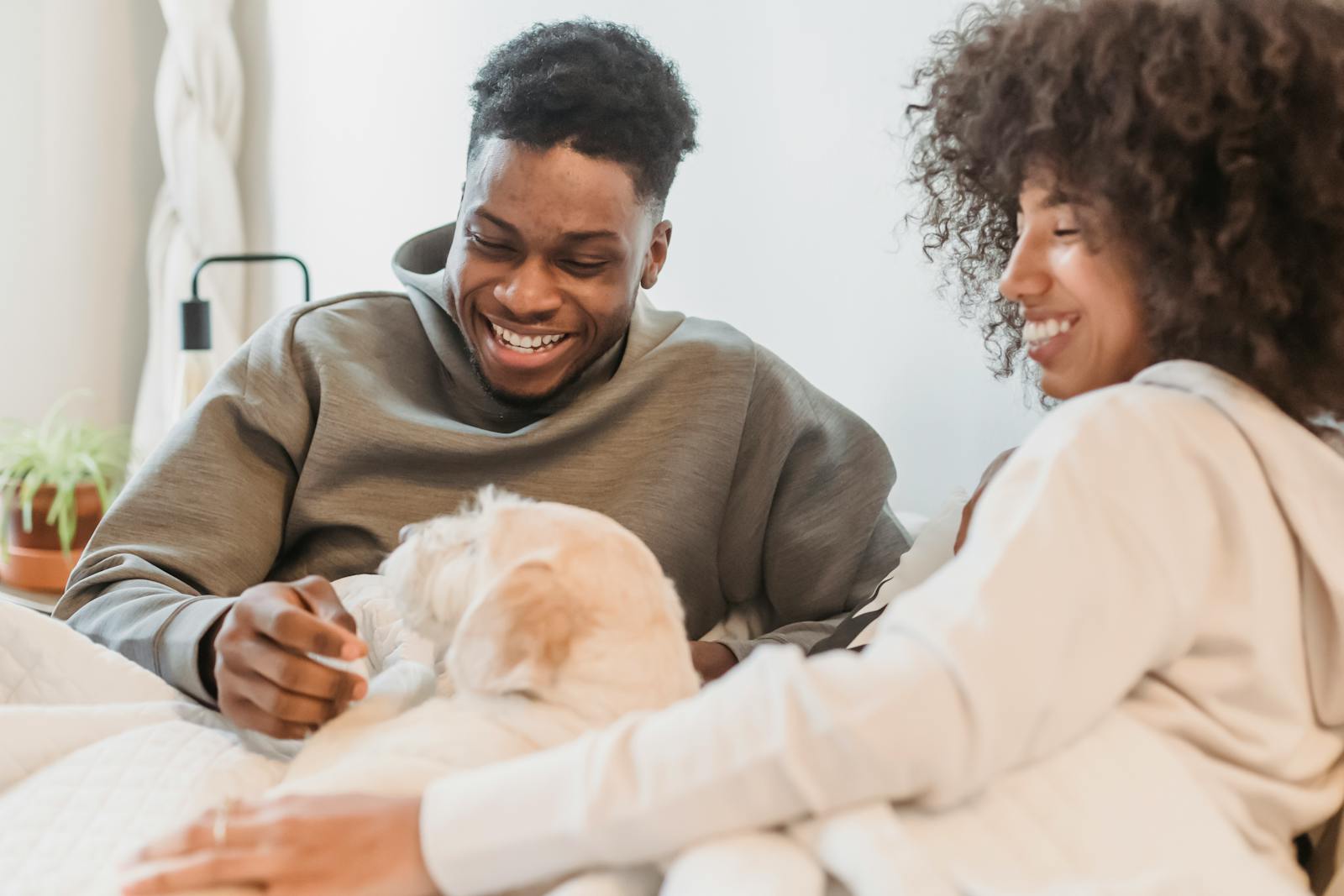 Happy African American man and woman in hoodies spending time with dog while resting and smiling together
