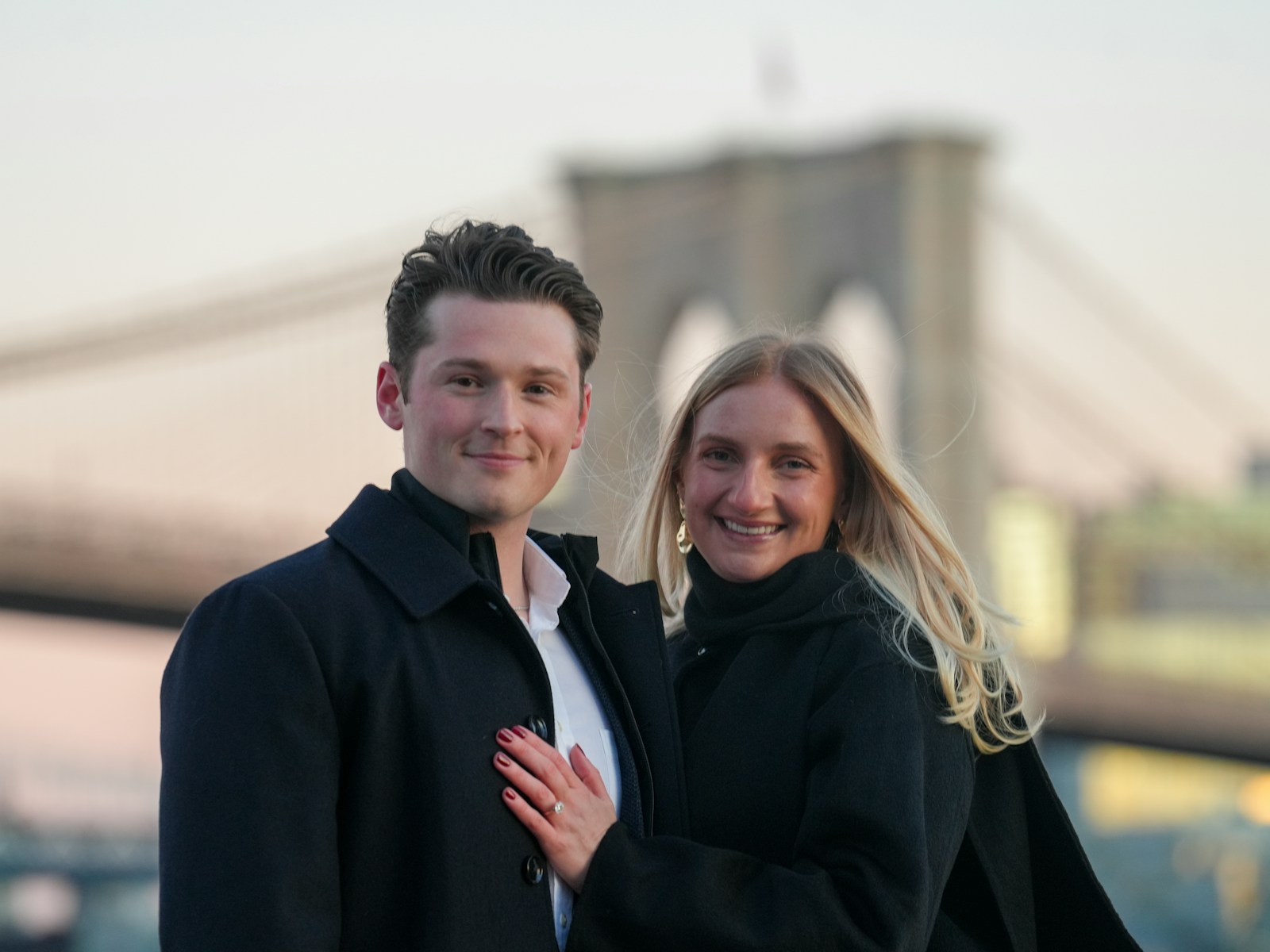 Couple posing in front of brooklyn bridge at sunset