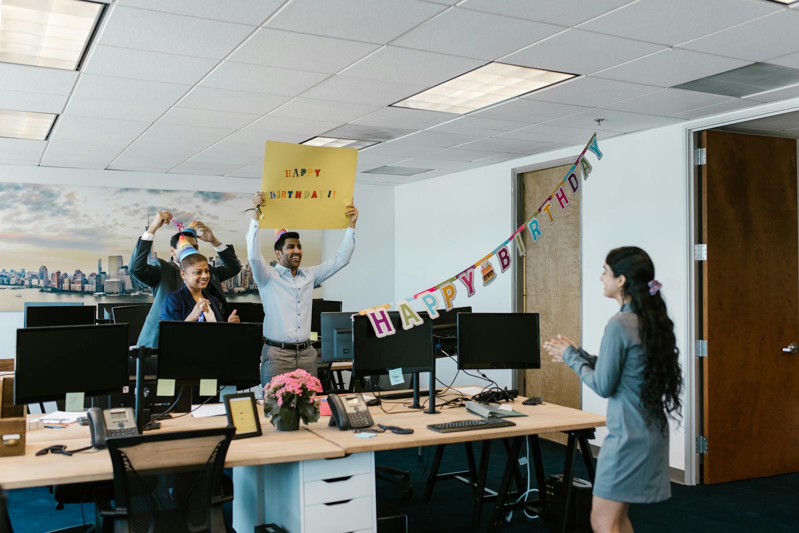 A joyful office birthday celebration with colleagues surprising a coworker with a banner and decorations.