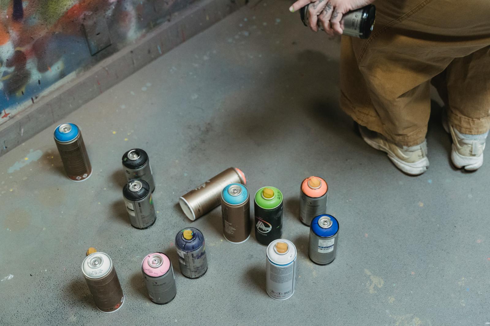Various colored spray cans on the floor with artist in the background.