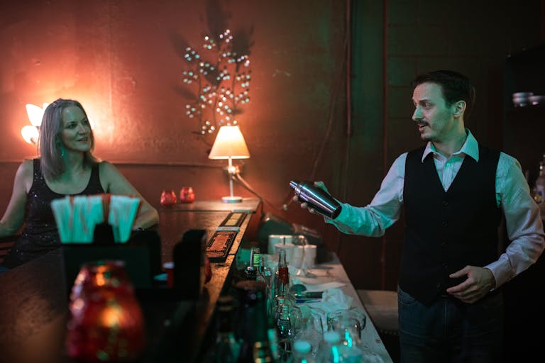 A bartender prepares a cocktail for a woman at a stylish bar, creating a vibrant nightlife scene.