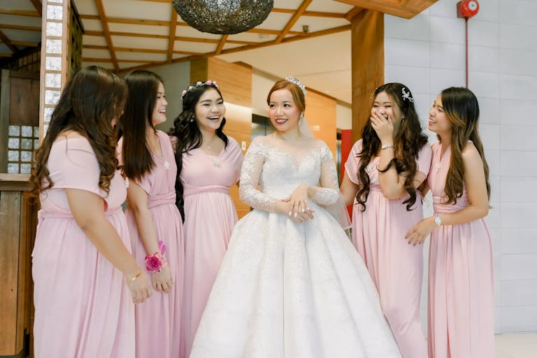 A bride and her bridesmaids share a joyful moment indoors, showcasing elegant wedding attire in a cheerful celebration.