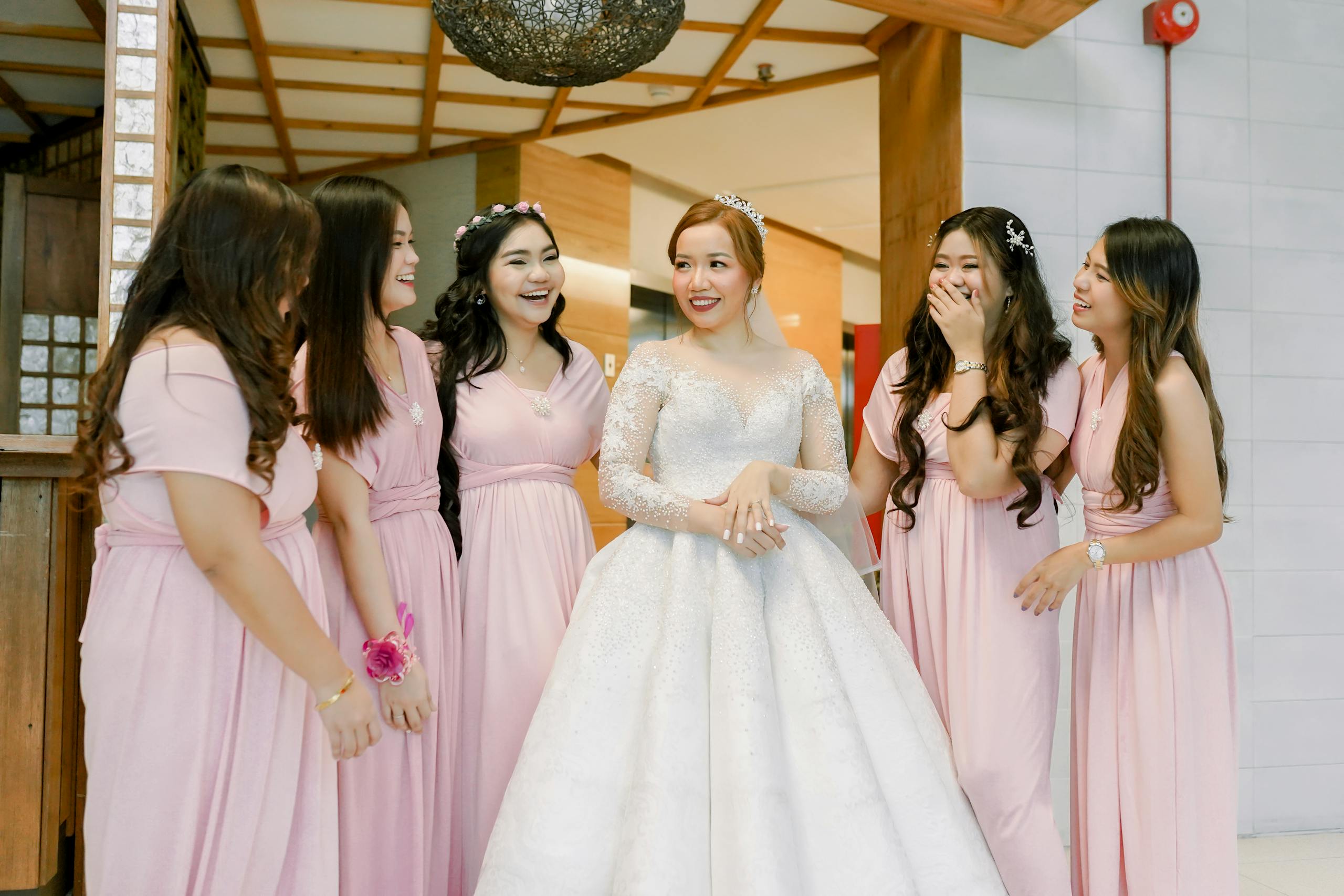 A bride and her bridesmaids share a joyful moment indoors, showcasing elegant wedding attire in a cheerful celebration.