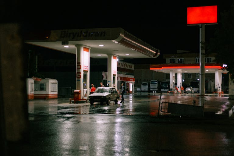 A car and people at a brightly lit gas station during the night.