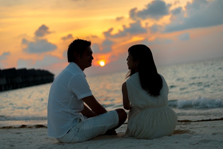 A couple sitting on a sandy beach, enjoying a beautiful sunset over the ocean.