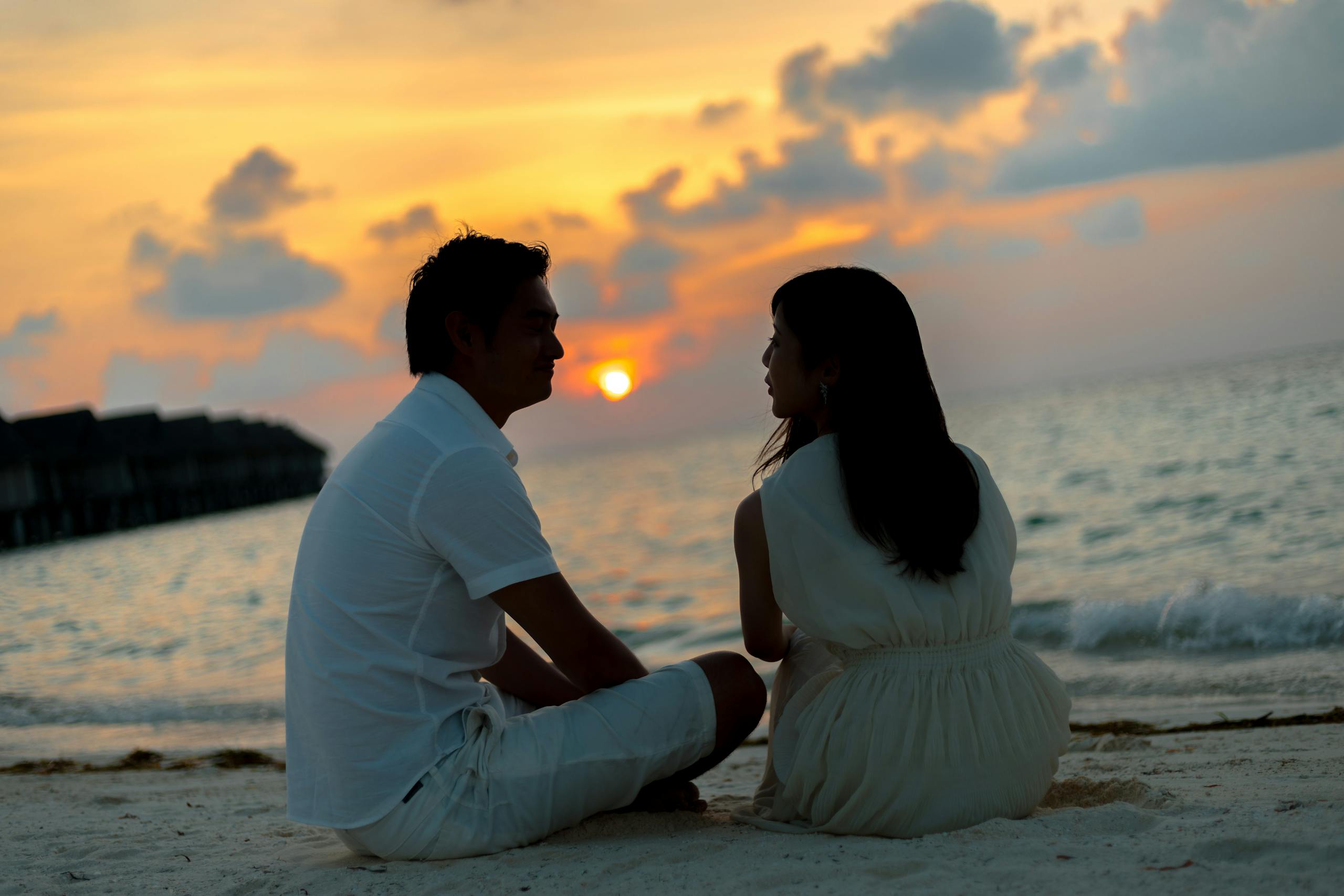 A couple sitting on a sandy beach, enjoying a beautiful sunset over the ocean.