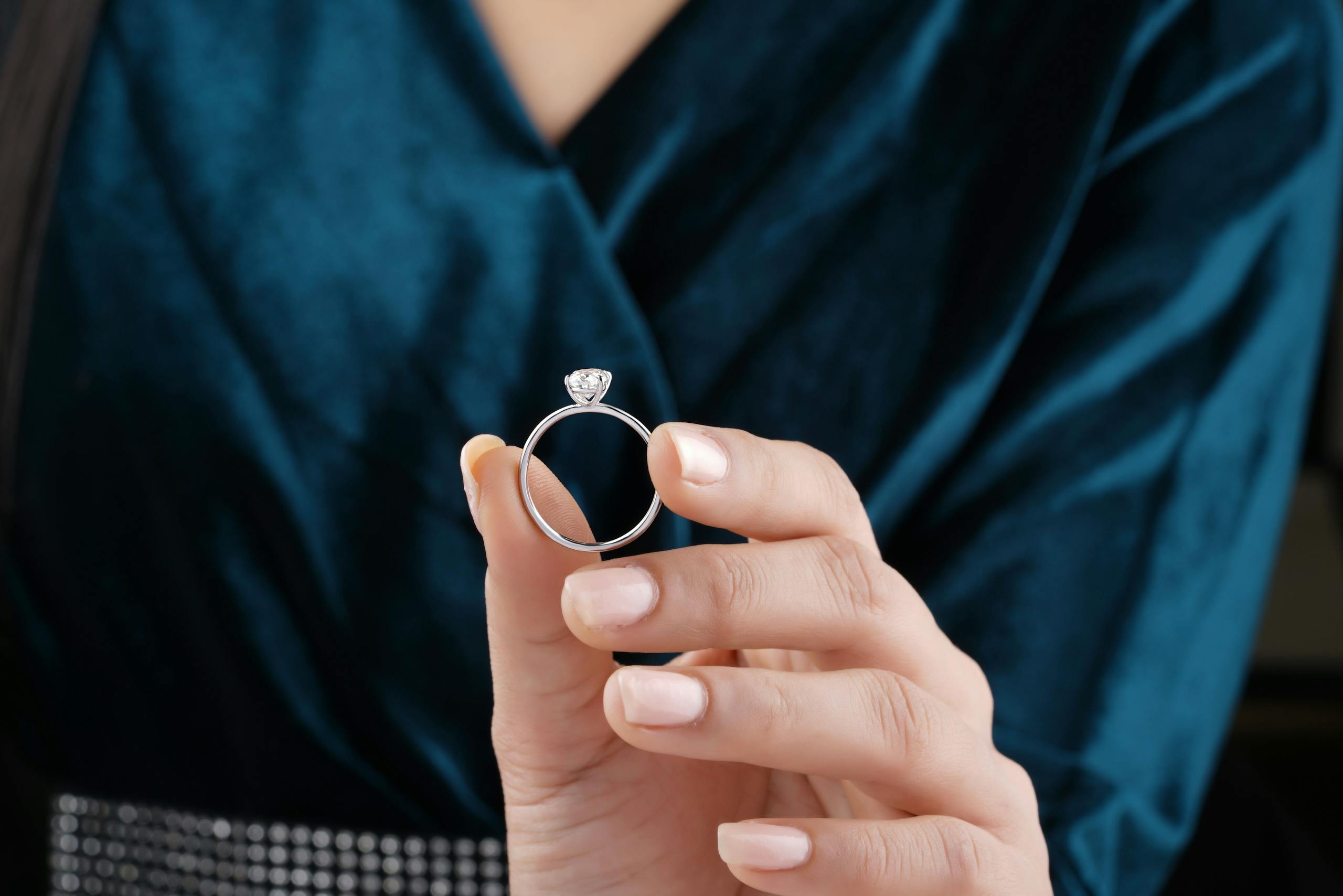 A detailed view of a hand holding a diamond solitaire engagement ring.