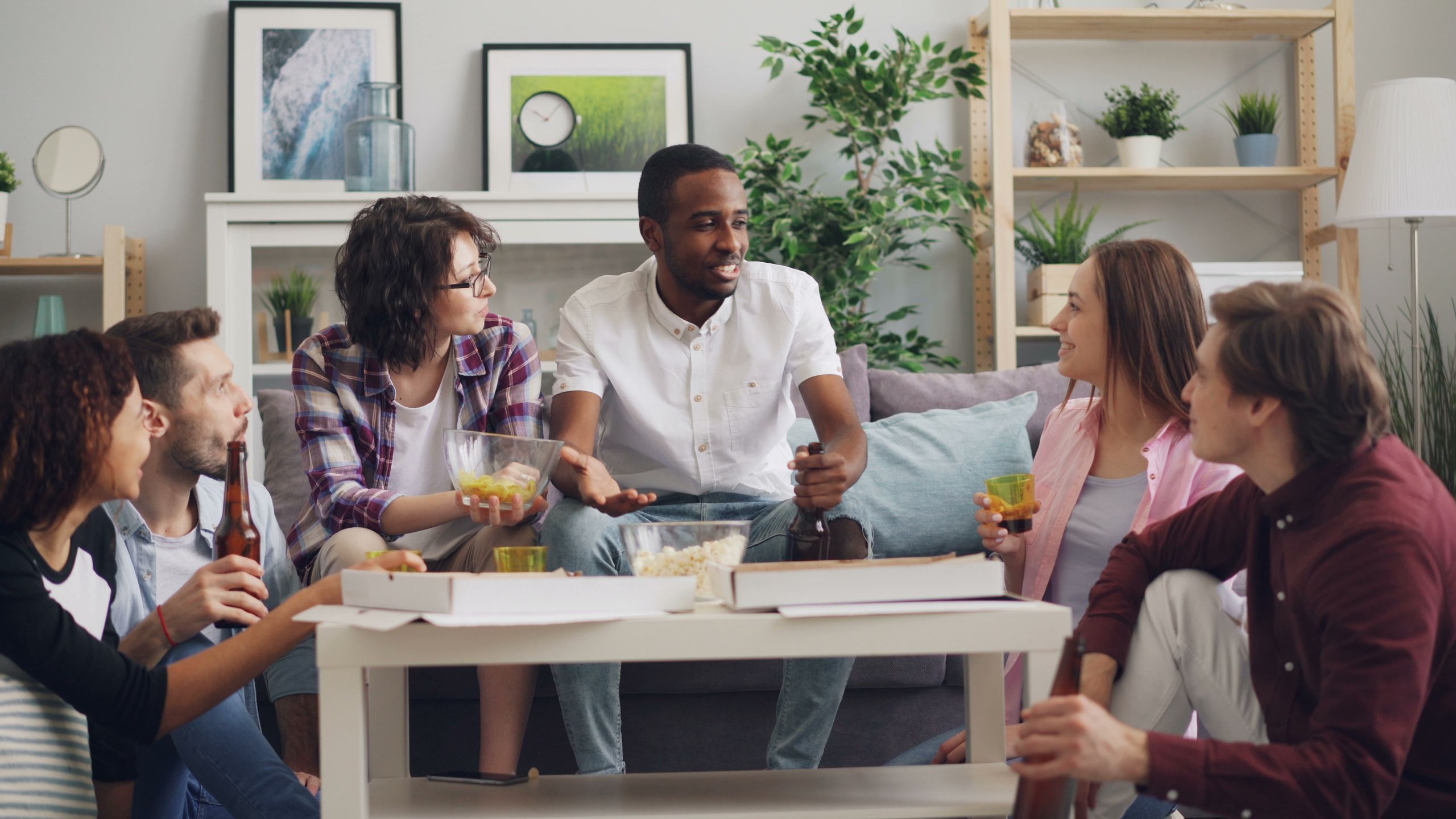 A diverse group of friends enjoying snacks and drinks indoors with smiles and conversation.