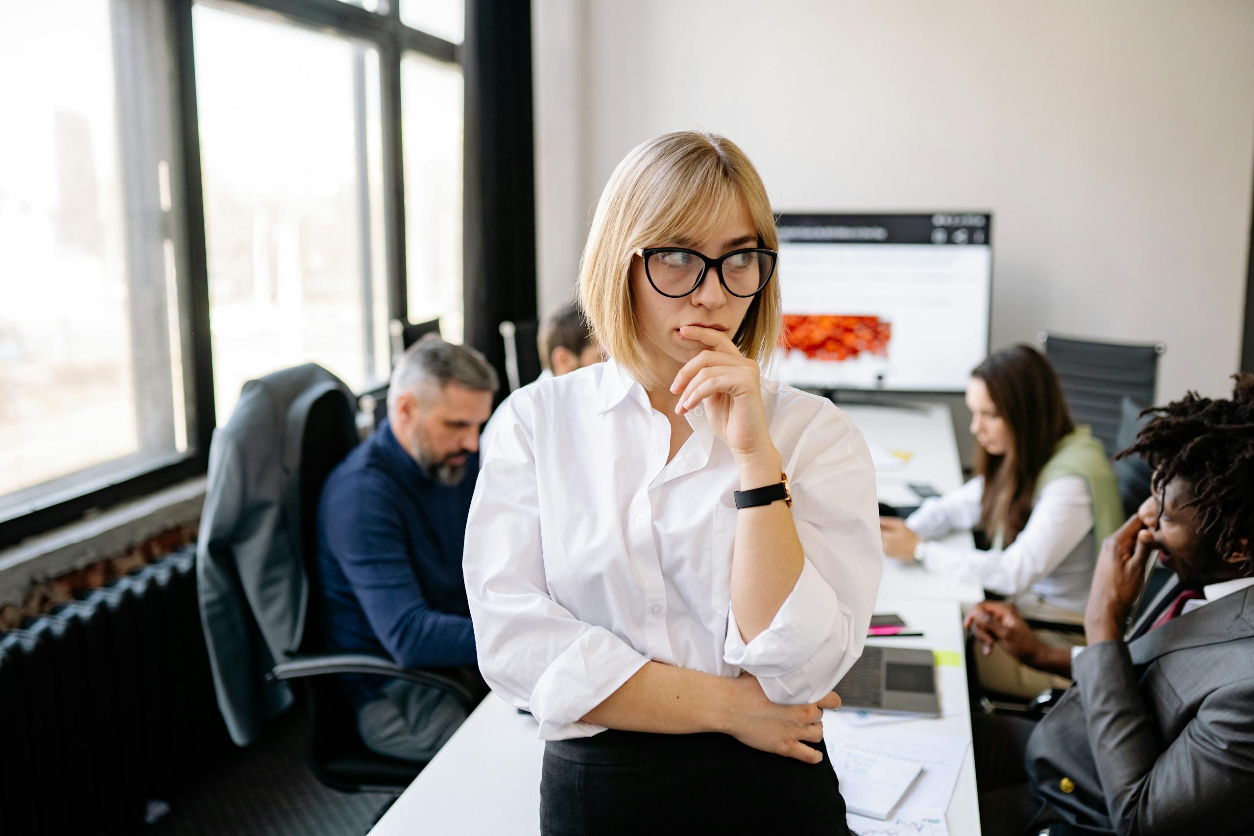 A focused businesswoman thinking during a team meeting in a modern office.