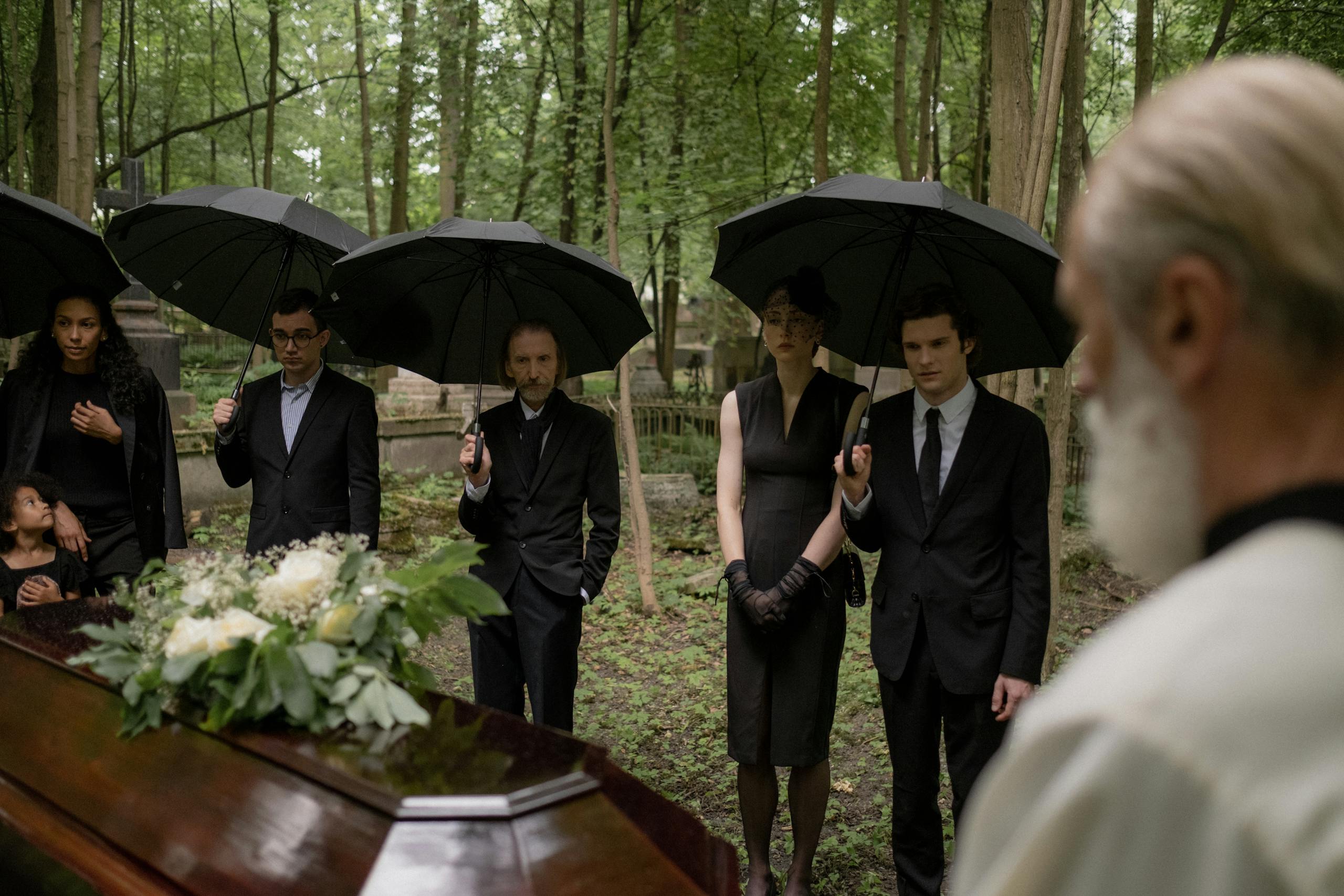 A group mourns during a funeral gathering in a forest cemetery.
