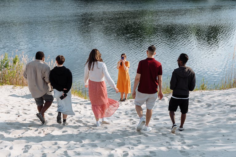 A group of friends enjoy a sunny day near a calm lake, capturing memories on a sandy beach.