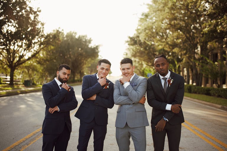 A group of stylish men in formal suits posing confidently on an outdoor road.
