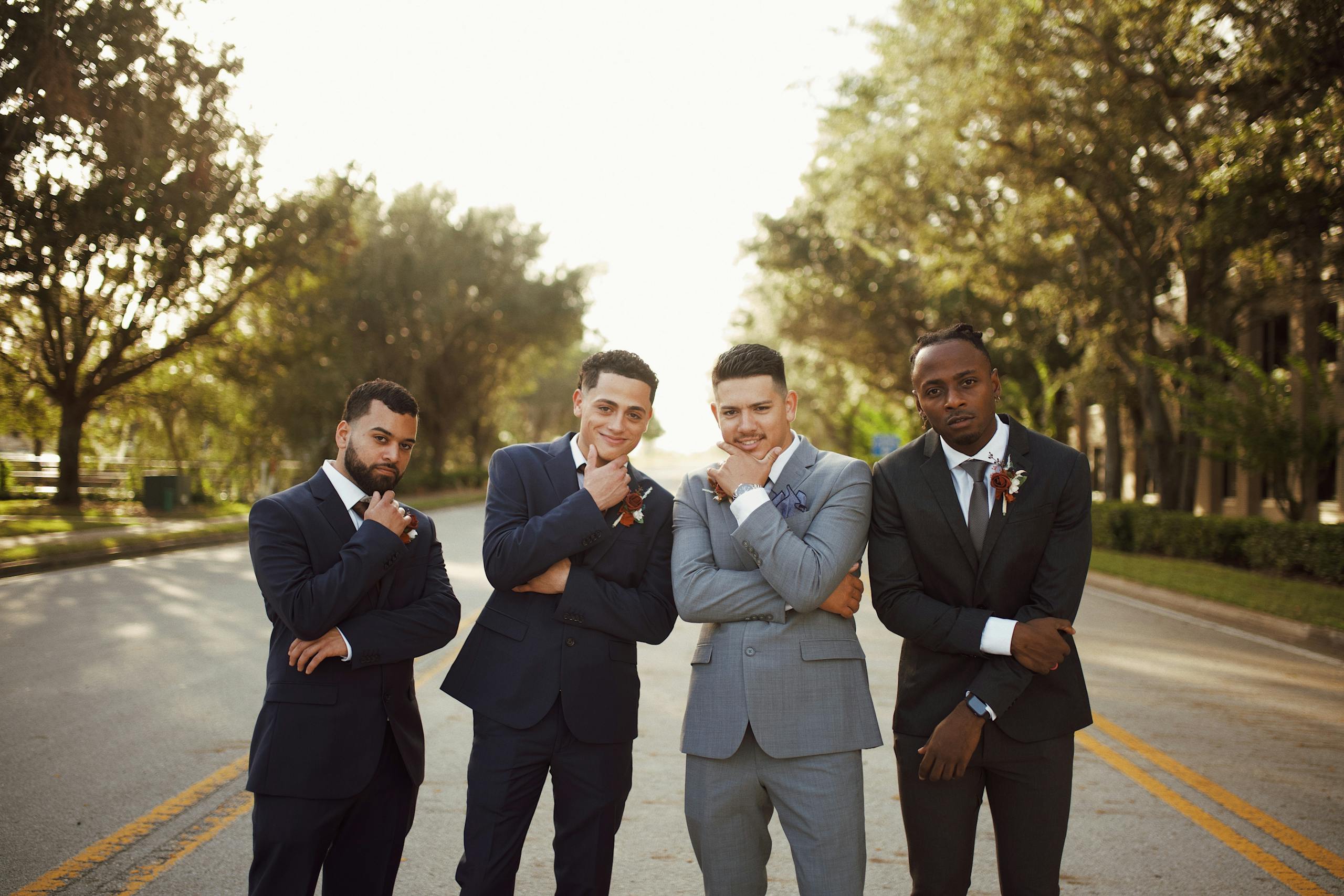 A group of stylish men in formal suits posing confidently on an outdoor road.