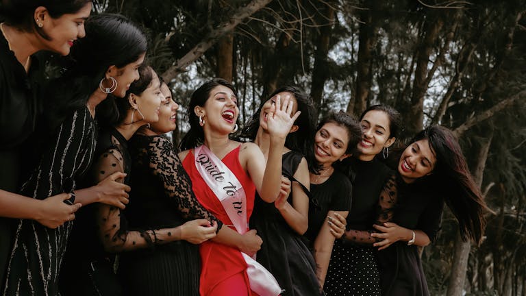 A group of women joyously celebrating outdoors with the bride-to-be wearing a sash.