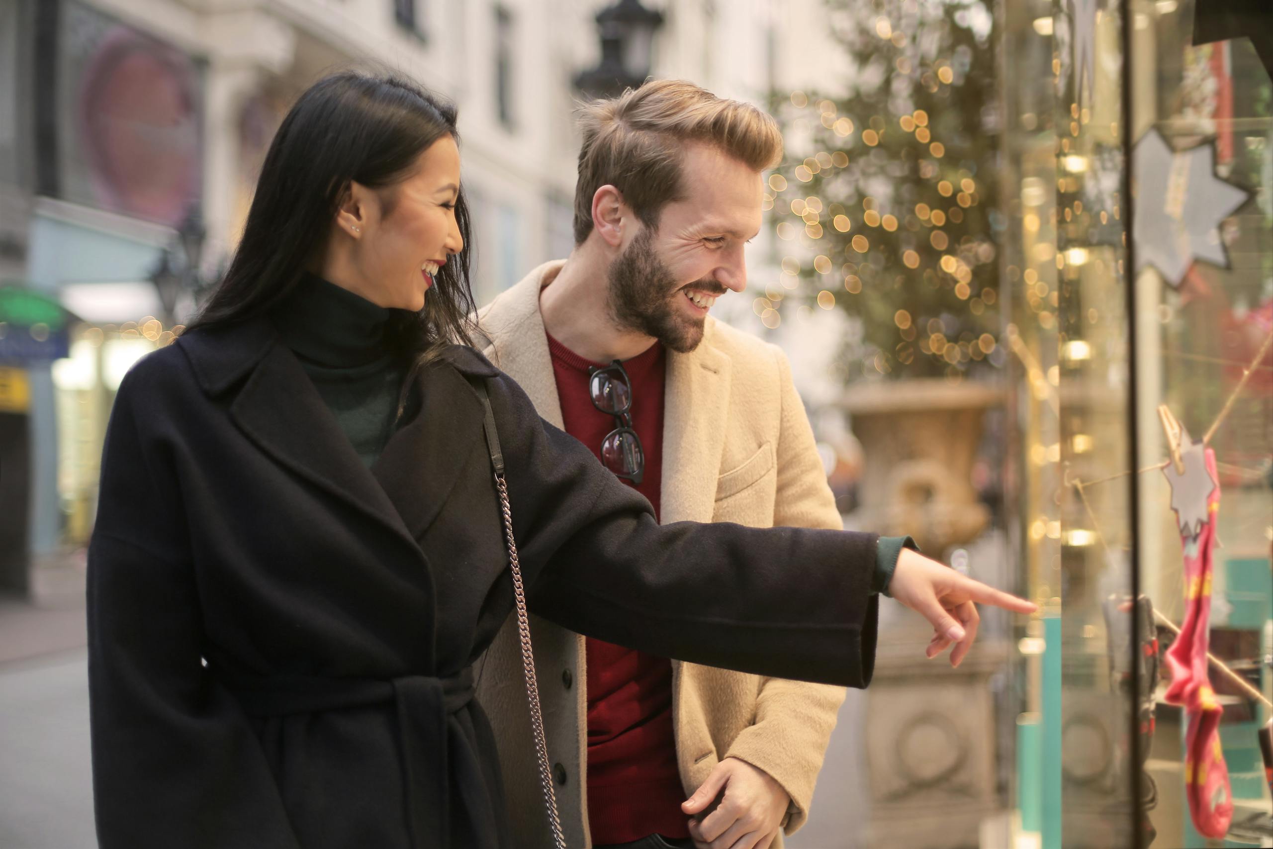 A happy couple window shopping together in an urban street setting during daylight.