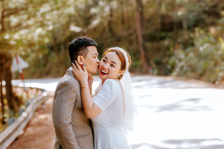 A joyful bride and groom smiling in a romantic embrace outdoors on a sunny day.