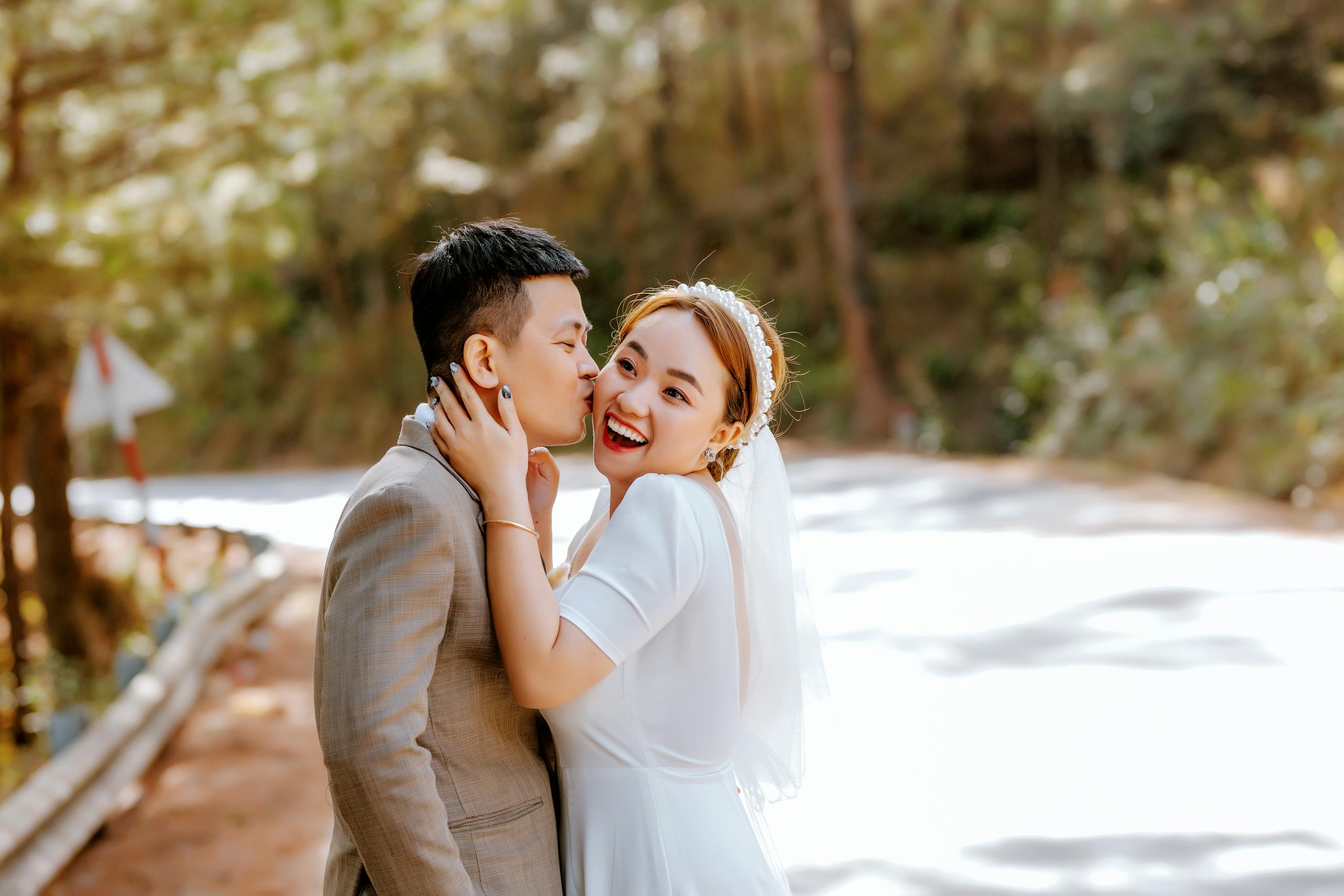 A joyful bride and groom smiling in a romantic embrace outdoors on a sunny day.