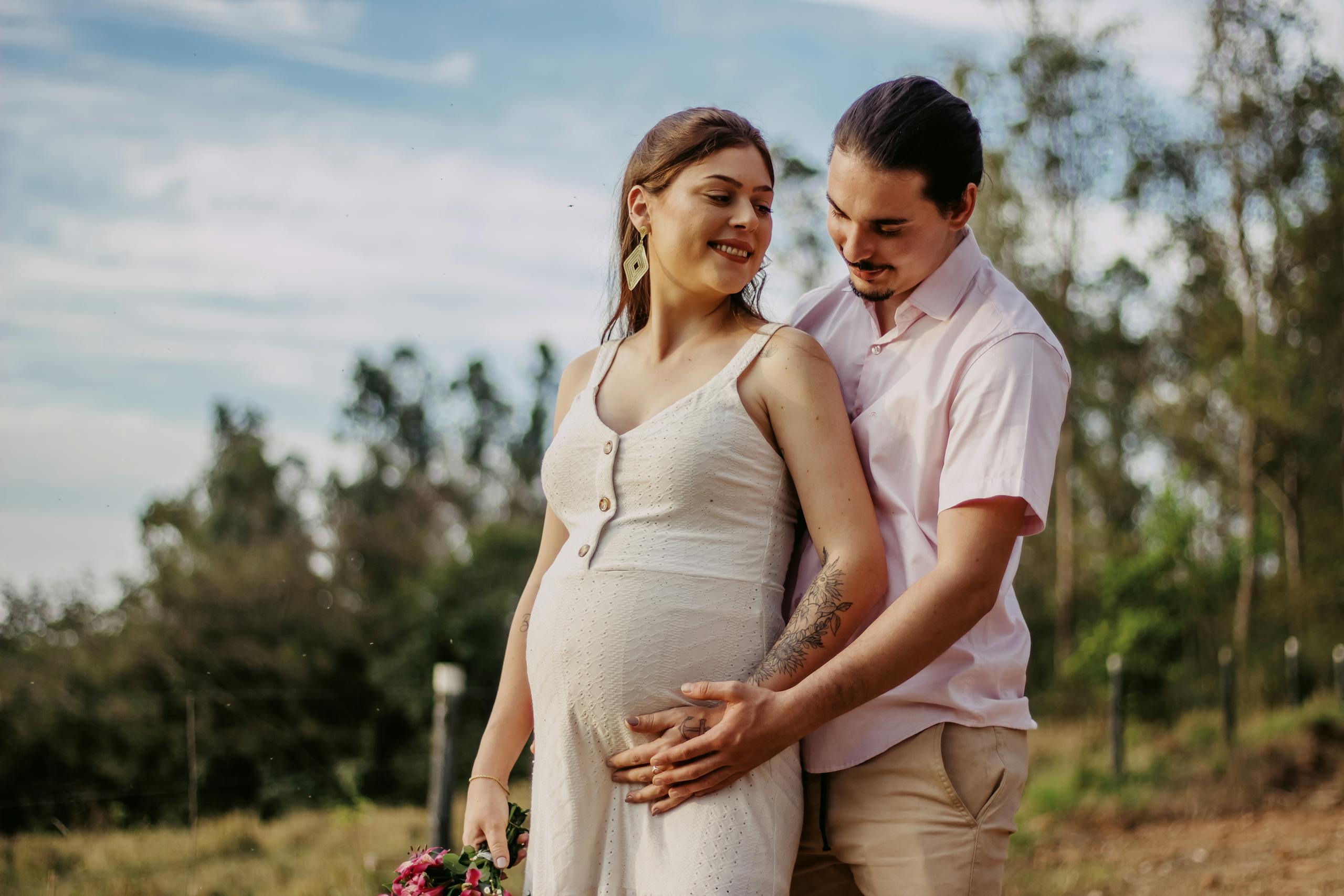 A joyful couple expecting a baby, embracing outdoors, showcasing love and anticipation.