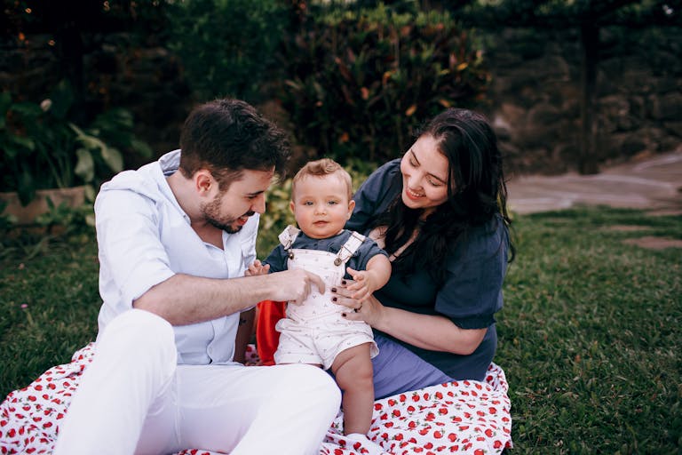 A joyful family with a baby sits outdoors on a picnic blanket, enjoying quality time together.