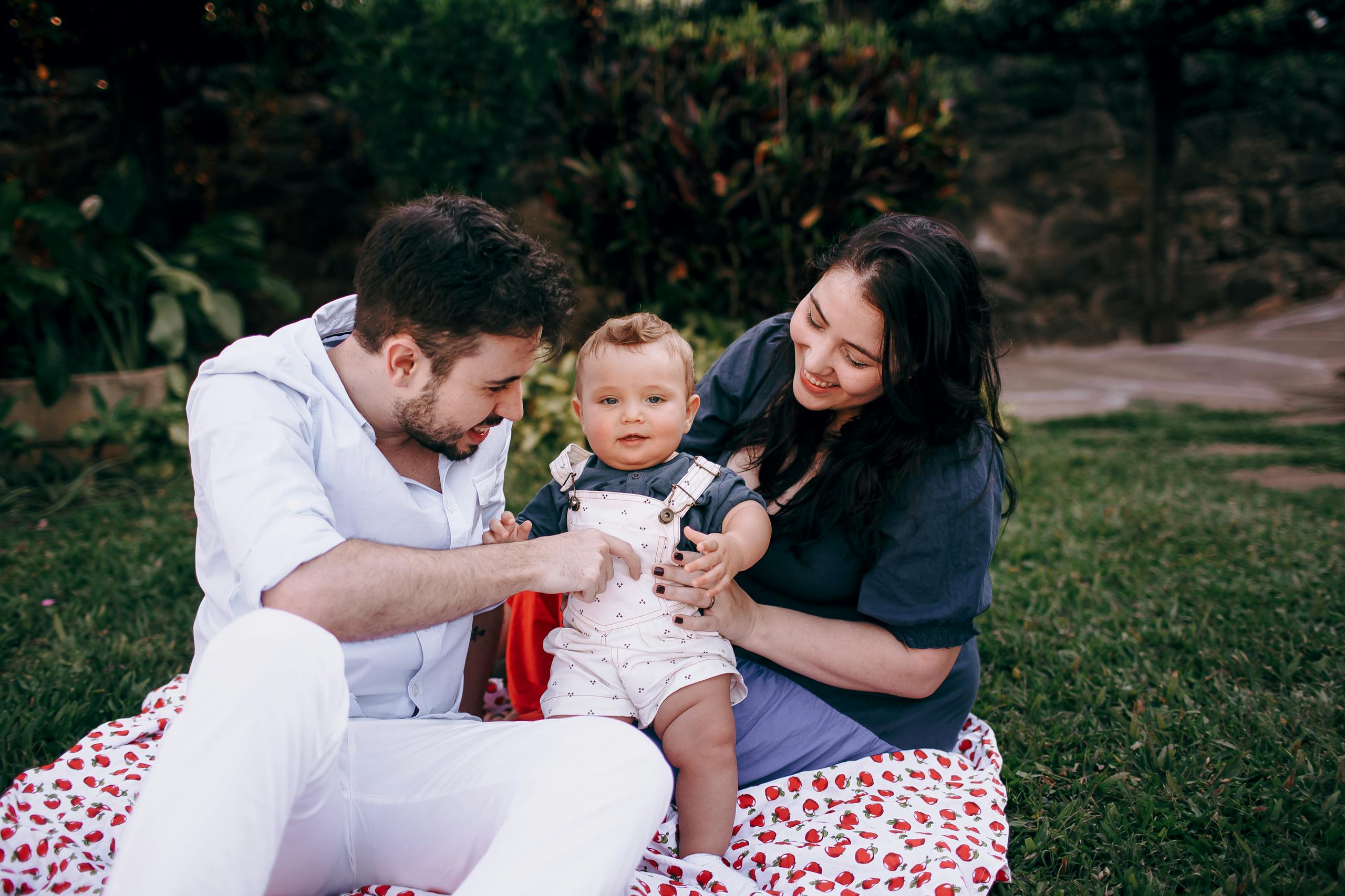 A joyful family with a baby sits outdoors on a picnic blanket, enjoying quality time together.