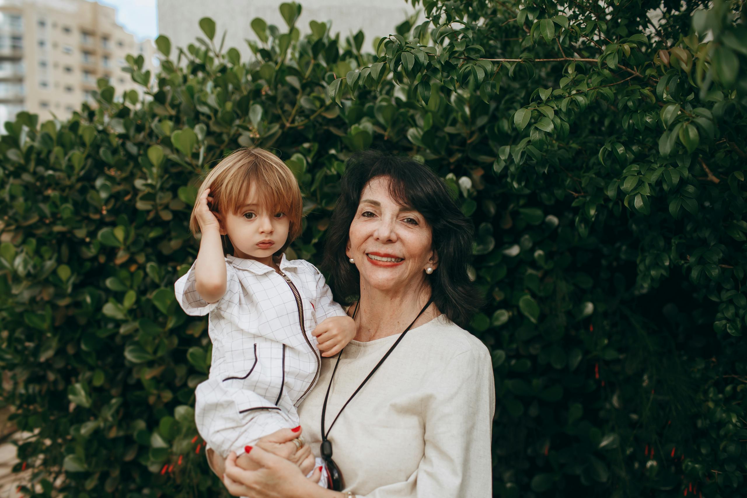 A loving grandmother with her grandchild smiling outdoors in a lush garden setting.