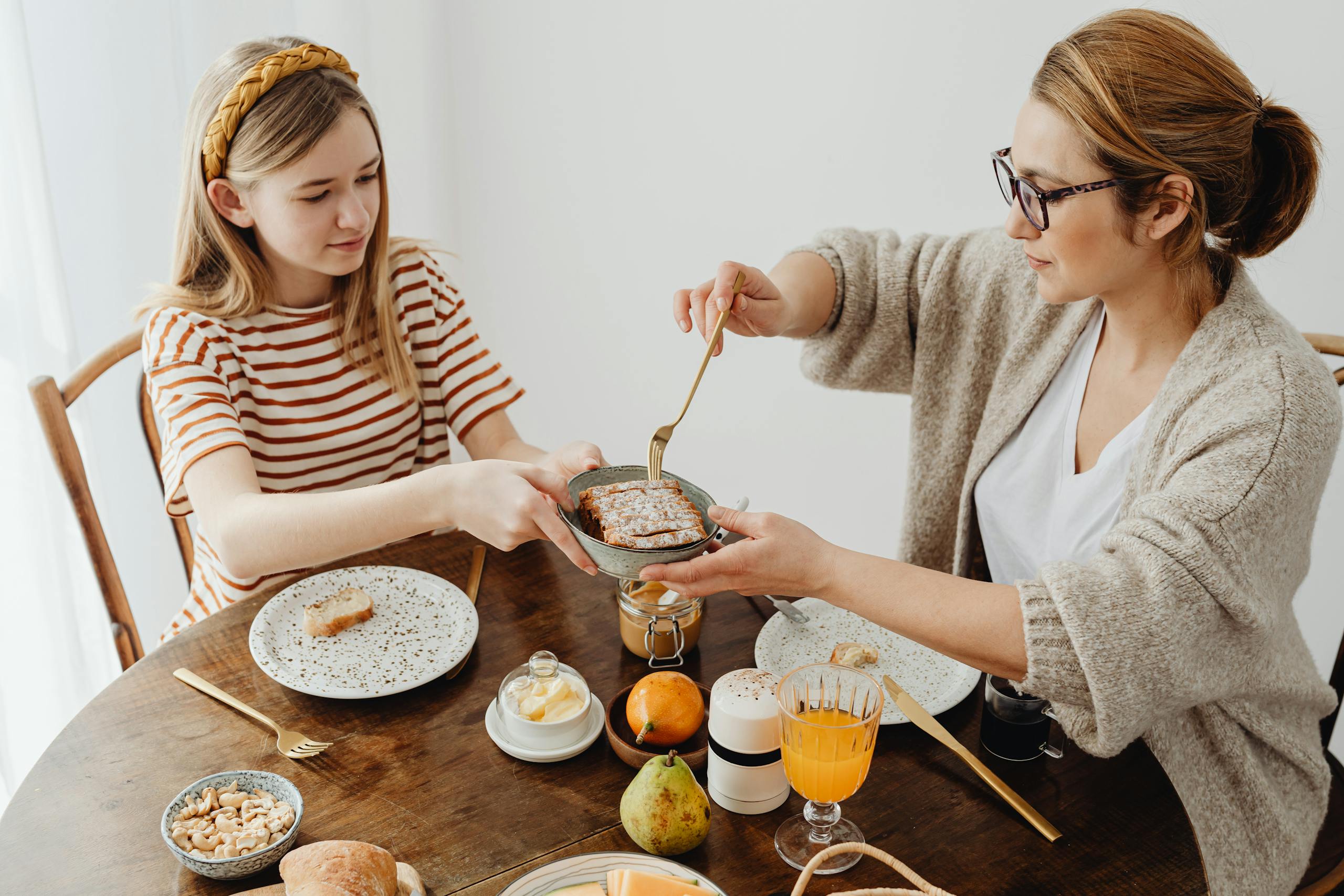 A mother and daughter enjoying a cozy breakfast with toast and juice at the dining table.