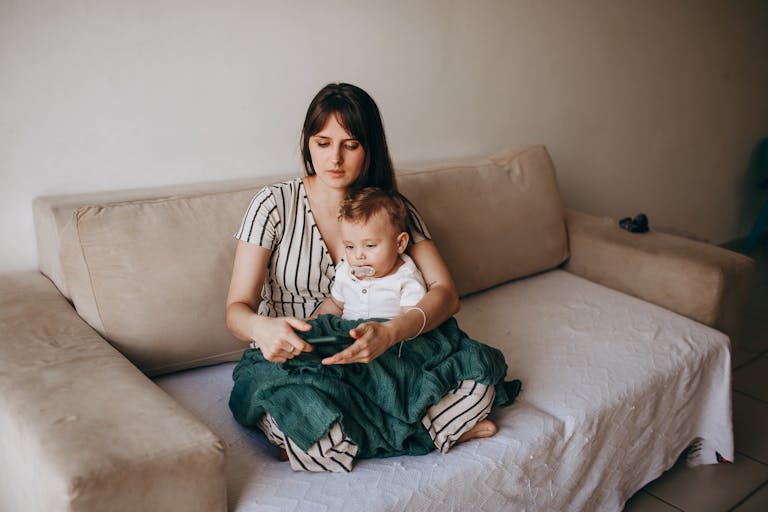 A mother and her baby seated together on a cozy sofa in a warm, loving home environment.