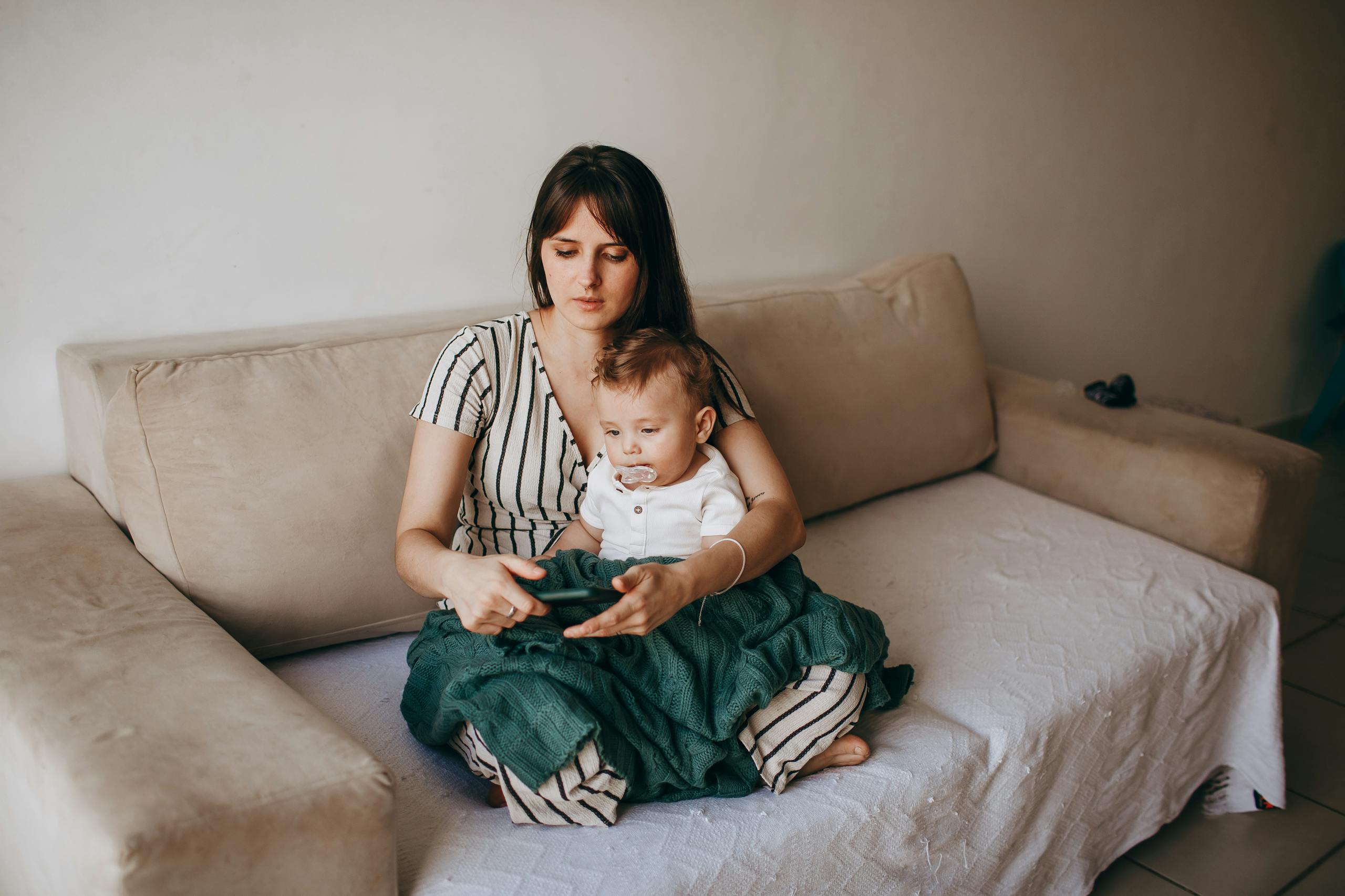 A mother and her baby seated together on a cozy sofa in a warm, loving home environment.