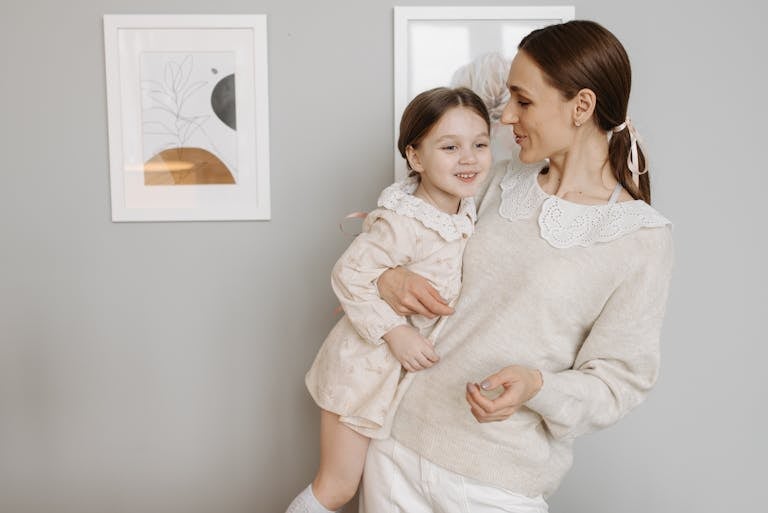 A mother lovingly holds her daughter, both wearing casual and cozy clothing indoors.