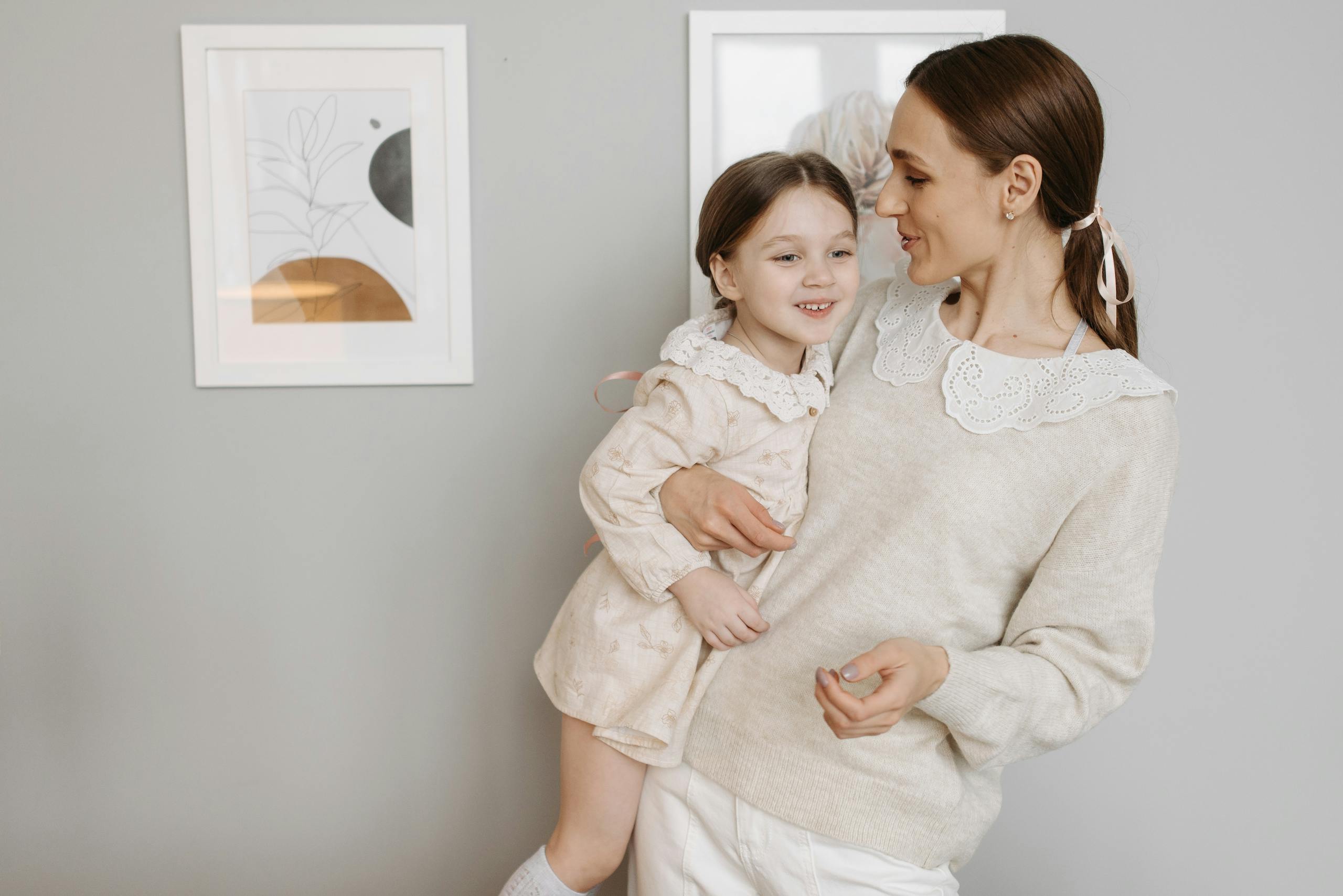 A mother lovingly holds her daughter, both wearing casual and cozy clothing indoors.