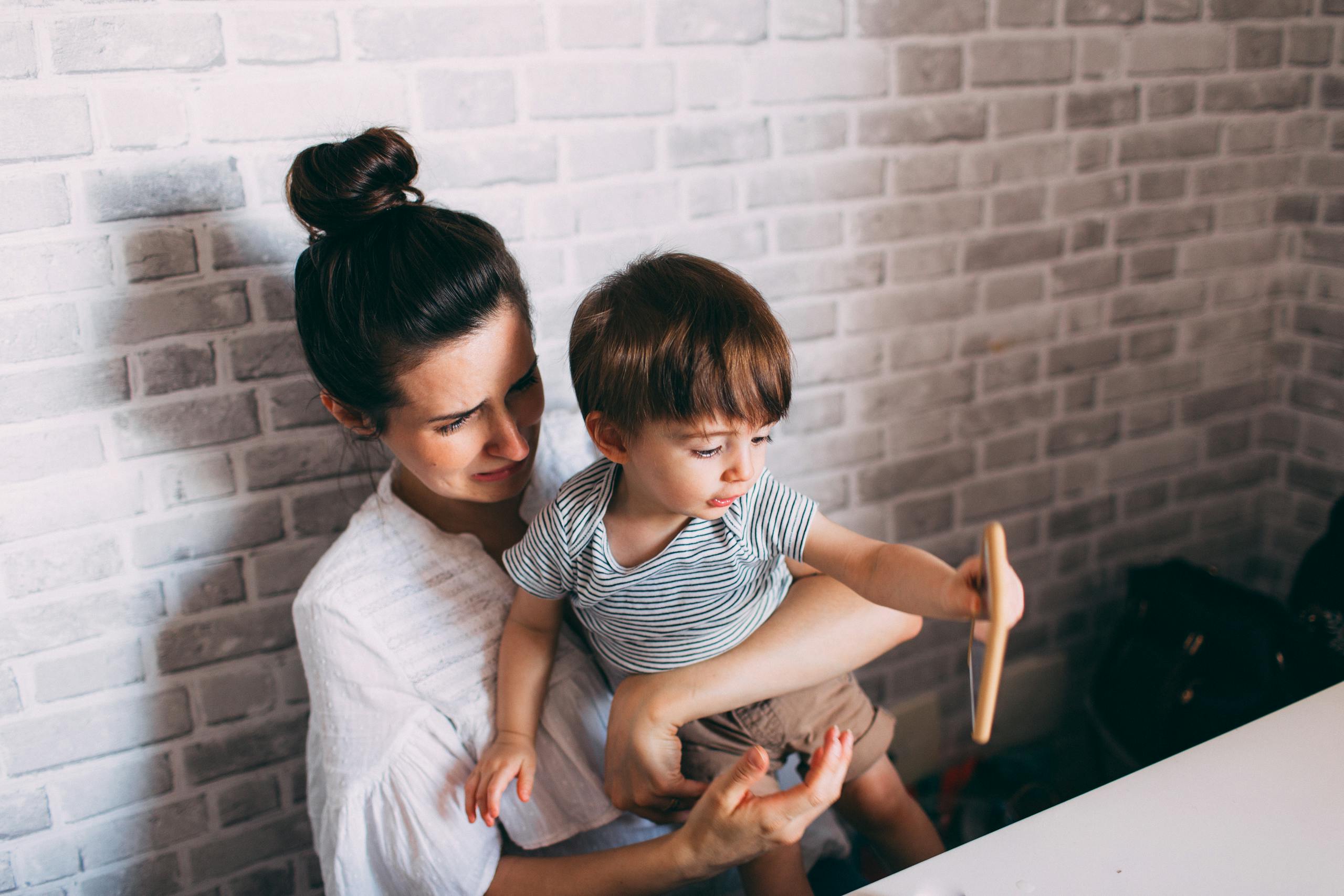 A mother lovingly holds her toddler indoors, sharing a joyful moment together.