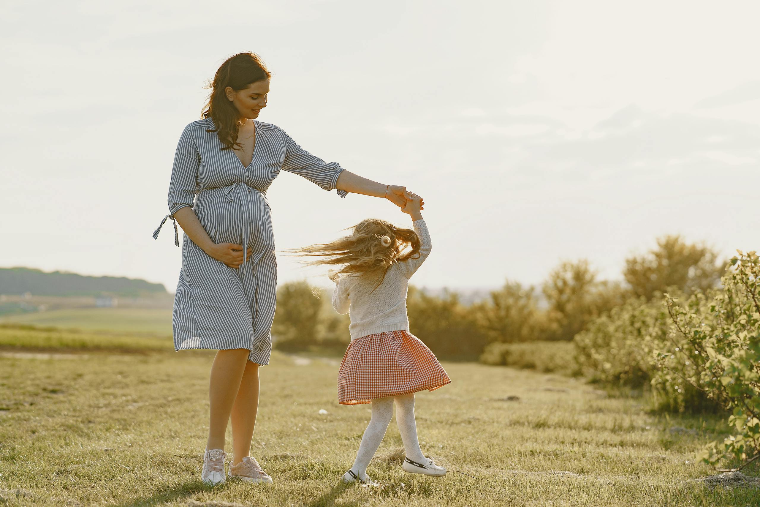A pregnant mother and her daughter enjoying a joyful moment outdoors in the sunshine.