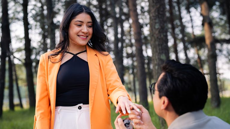 A romantic moment captured with a man proposing outdoors in a sunlit forest setting.
