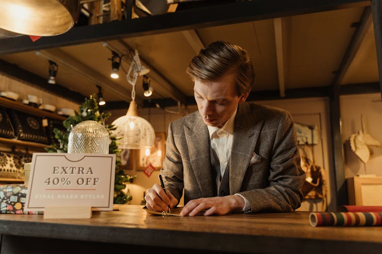 A salesman in a suit writing at a store counter during a Christmas sale.