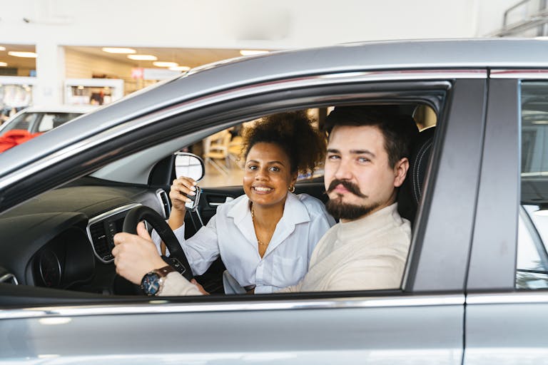 A smiling couple sitting inside a new car, holding the key and looking pleased.
