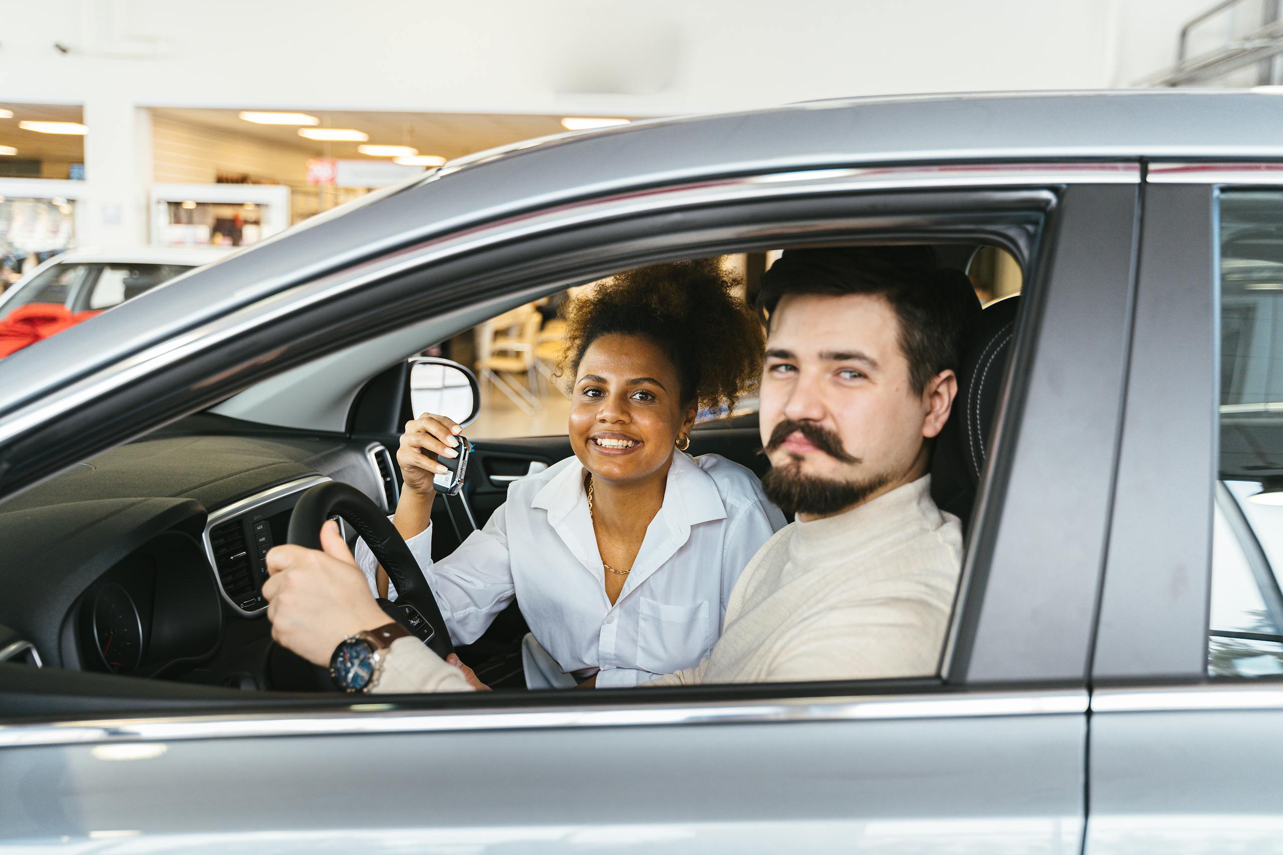 A smiling couple sitting inside a new car, holding the key and looking pleased.