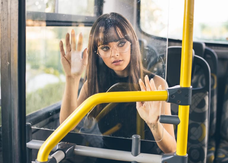 A stylish woman wearing eyeglasses sitting on a bus, gazing outside. Urban travel scene.