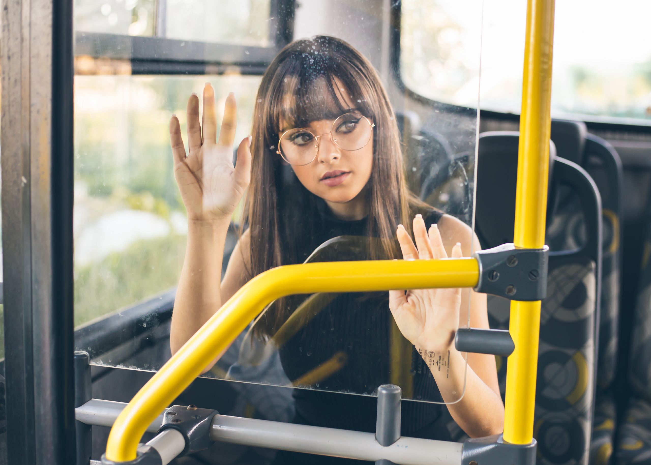 A stylish woman wearing eyeglasses sitting on a bus, gazing outside. Urban travel scene.